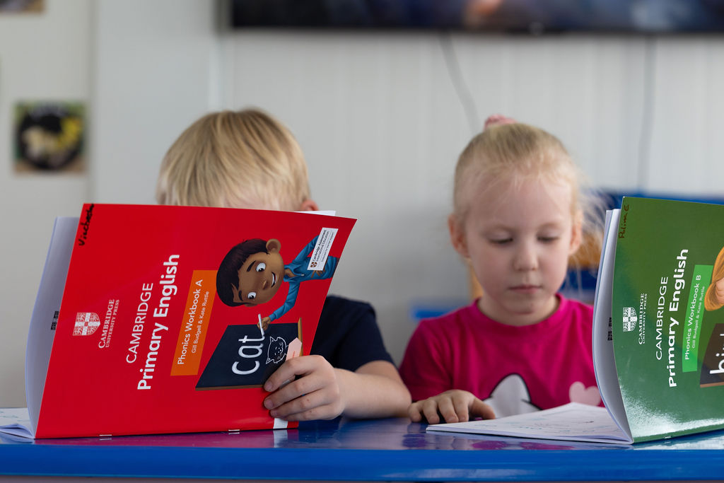 Children looking at Cambridge Primary English phonics workbooks at Golden Oak.