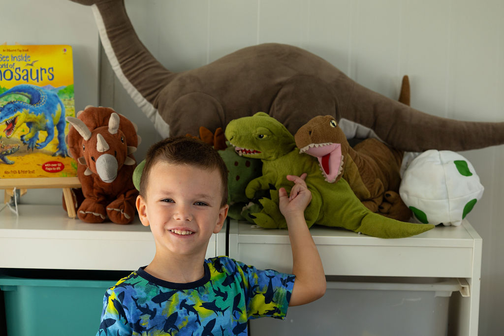 A child beside dinosaur books and soft toys in a Golden Oak classroom.
