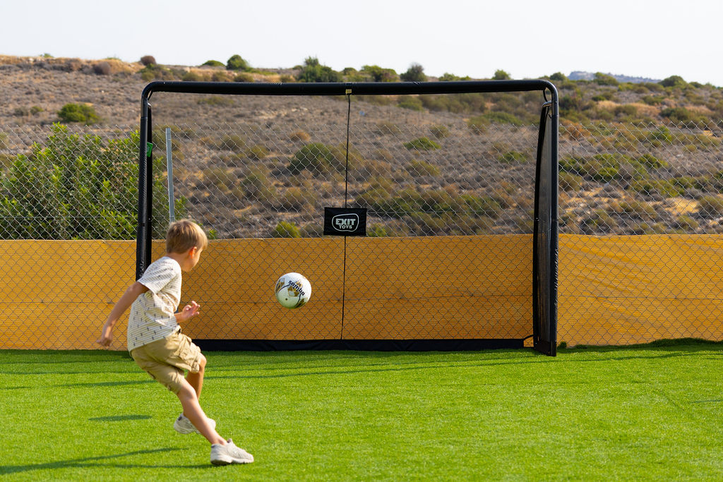 A child kicking a football towards a goal in Golden Oak’s outdoor play area.
