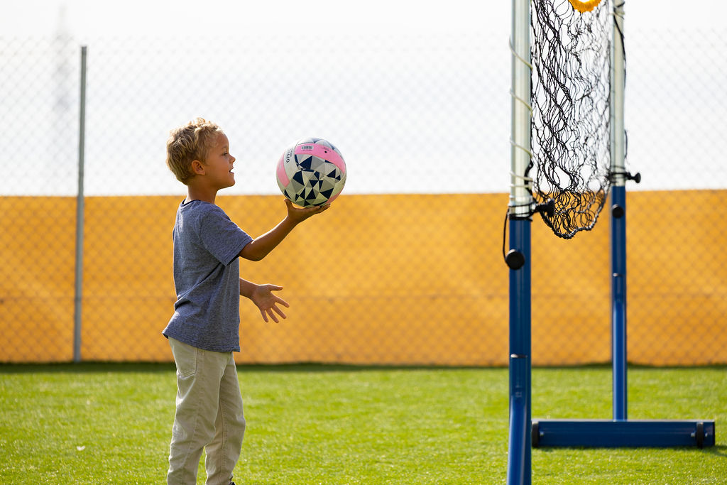 A Golden Oak pupil playing with a ball beside an outdoor basketball hoop.