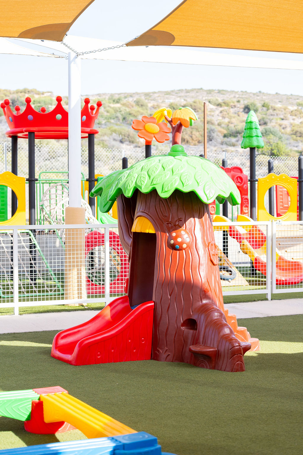 A tree-shaped playhouse and slide in Golden Oak’s shaded outdoor play area.