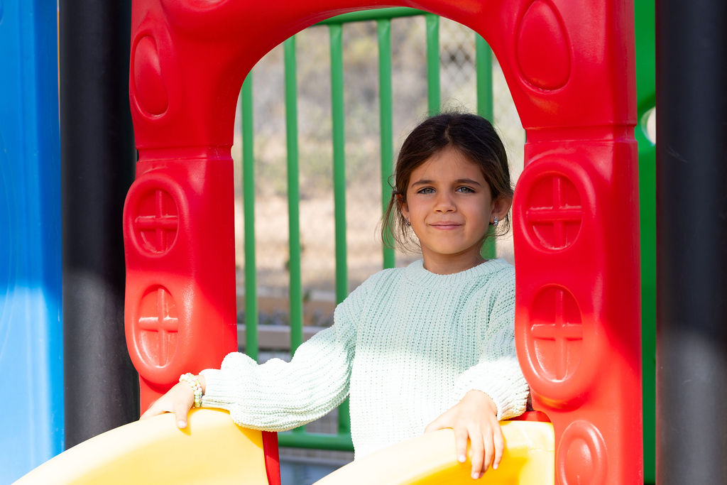 A child sitting on a yellow slide beside red play equipment at Golden Oak.