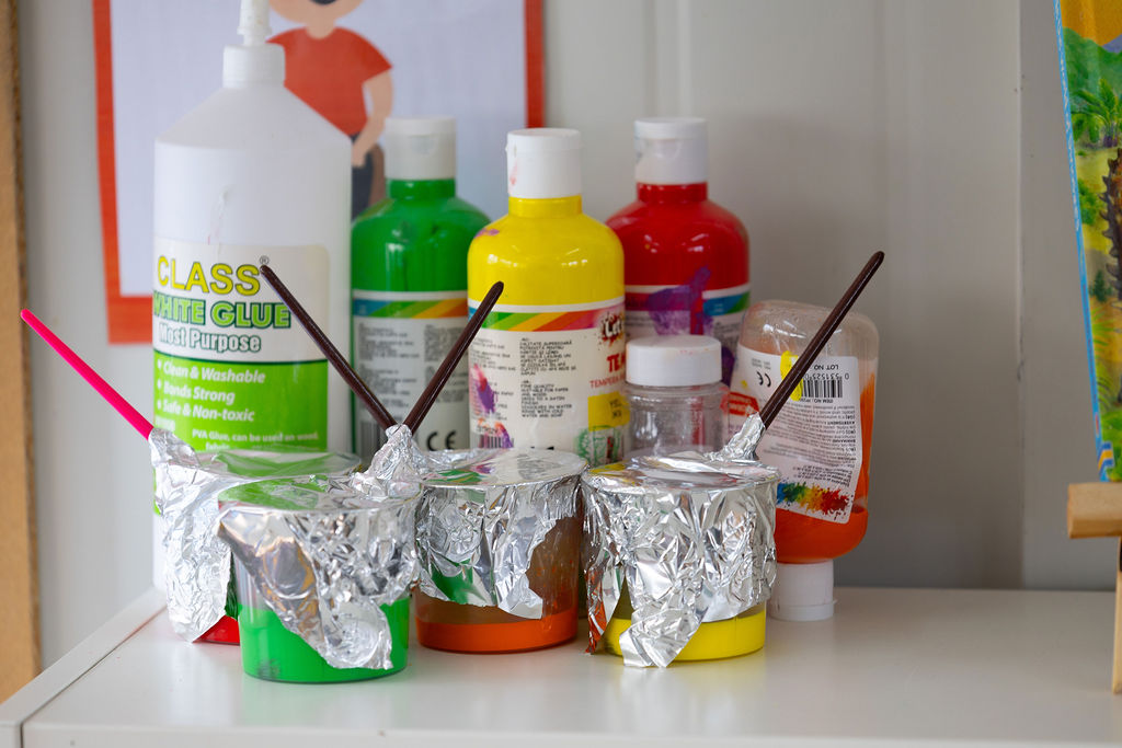Paint bottles and brushes arranged on a Golden Oak classroom table.